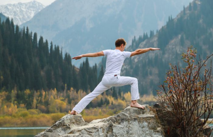 A man practices yoga on a background of mountains. Pose Virabhadrasana 2 or warrior